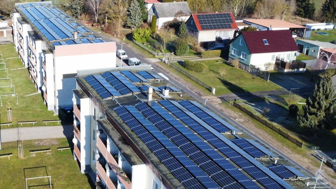 Luftaufnahme von mehreren Mehrfamilienhäusern mit großflächigen Photovoltaik-Anlagen auf den Dächern in einer Wohnsiedlung